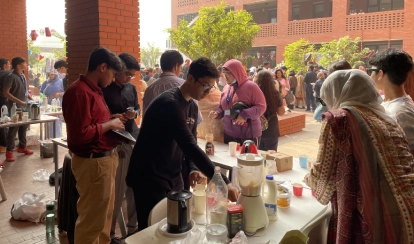 Students and visitors gather in a courtyard at the Aga Khan Academy Dhaka during a service-learning fundraising event, with students running stalls and preparing refreshments.